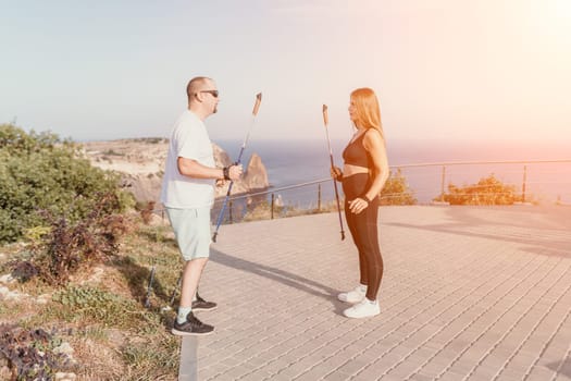 Happy Middle aged couple or friends practicing nordic walking in park near sea. Mature couple with trekking poles walking, practicing Nordic walking outdoors. Aging youthfully and sport concept.