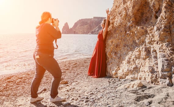 Side view a Young beautiful sensual woman in a red long dress posing on a rock high above the sea during sunrise. Girl on the nature on blue sky background. Fashion photo.