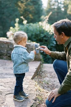 Dad gives a soft toy to sniff dandelions in the hand of a little girl. High quality photo