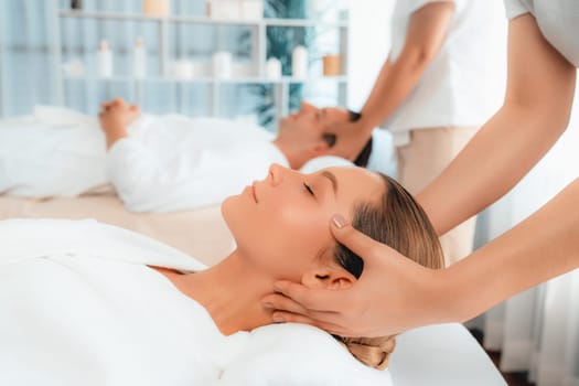 Caucasian couple enjoying relaxing anti-stress head massage and pampering facial beauty skin recreation leisure in dayspa modern light ambient at luxury resort or hotel spa salon. Quiescent