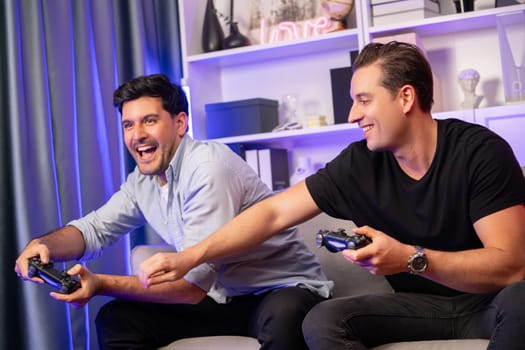 Winner and loser players of buddy friend gamers playing video game on TV using joysticks in studio room with neon blue light. Comfy living indoor at home place with cheerful fighting winner. Sellable.