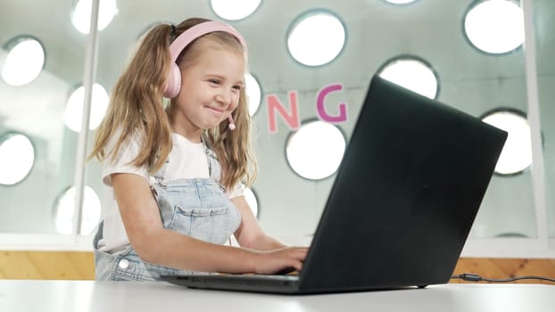 Young student working on laptop or studying in online classroom. Caucasian girl typing on laptop while doing homework or listening music.Little kid wearing headphone. Creative learning. Erudition.