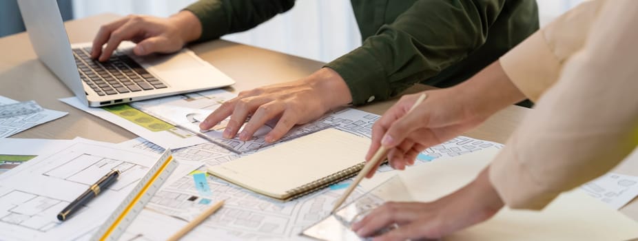 Professional engineer team discussion about house design on meeting table with architectural equipment and blueprint scatter around at modern office. Focus on hand. Closeup. Delineation.