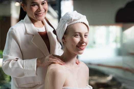 Attractive caucasian women receives back massage with smile face by Thai professional masseur while sitting surrounded by peaceful spa environment. Healthy and beauty. Blurring background.Tranquility.