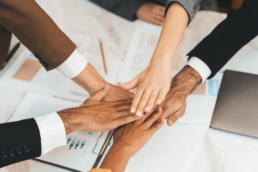 Top view of corporate diverse businesspeople putting hands together on meeting table with document scatter around at business meeting room. Represented unity, cooperation, collaboration. Ornamented.