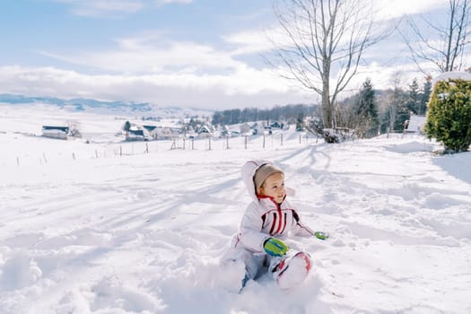 Little girl sits half-turned in a snowdrift and looks away. High quality photo