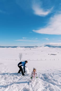 Little girl and her dad are making a snowman by rolling big snowballs across the lawn. High quality photo