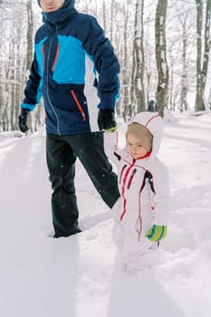 Dad and a little girl are walking holding hands through snowdrifts in the forest. Cropped. High quality photo