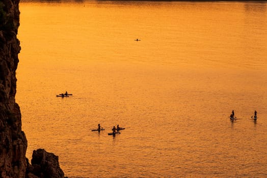 Adventurous people on a stand up paddle board is paddling during a bright and vibrant sunrise