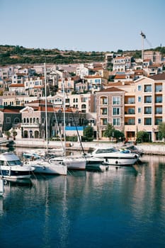 Rows of yachts are moored off the shore with colorful houses. Lustica Bay Marina, Montenegro. High quality photo