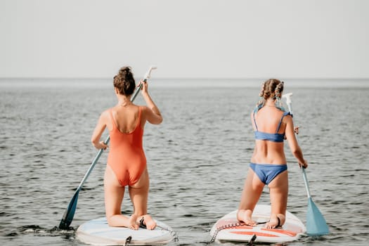 Woman sup yoga. Middle age sporty woman practising yoga pilates on paddle sup surfboard. Female stretching doing workout on sea water. Modern individual hipster outdoor summer sport activity