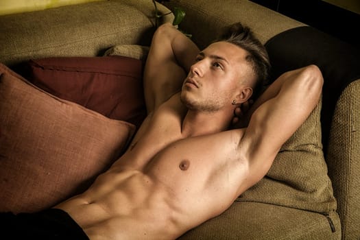 Shirtless sexy young man in panties relaxing on couch and looking away. Side view, close-up