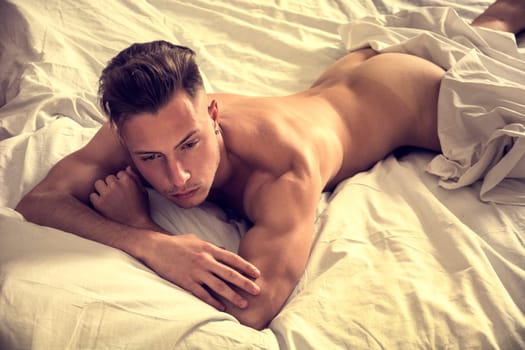 Totally naked sexy young man with muscular body on bed looking at camera