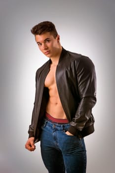 Handsome young muscleman with leather jacket on naked torso, isolated on white background in studio shot