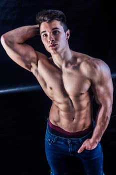 Handsome young muscular man shirtless wearing jeans, on dark background in studio shot