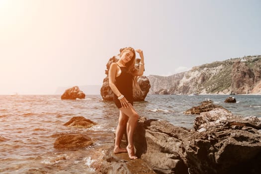 Woman travel sea. Young Happy woman in a long red dress posing on a beach near the sea on background of volcanic rocks, like in Iceland, sharing travel adventure journey