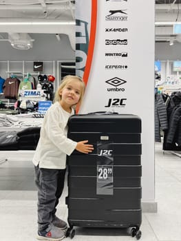 Little girl stands near a huge suitcase on wheels in a store. High quality photo