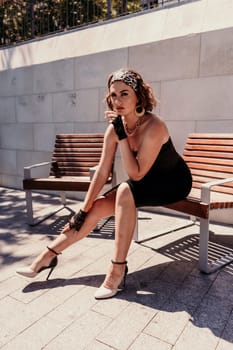 Portrait of a woman on the street. An attractive woman in a black dress is sitting on a bench outside