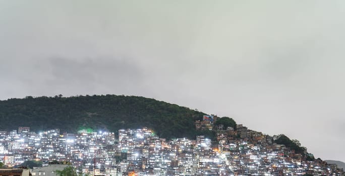 Illuminated favela on a hill highlights stark contrast in urban landscape.