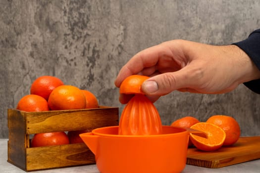 Man's hand squeezing an orange in a juicer with some ripe oranges in a still life with gray background, healthy living concept. Superfood rich in vitamin C