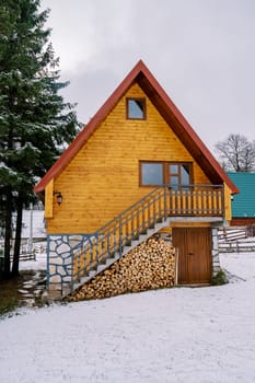 Two-story wooden cottage with a woodpile under the steps in a snowy forest. High quality photo