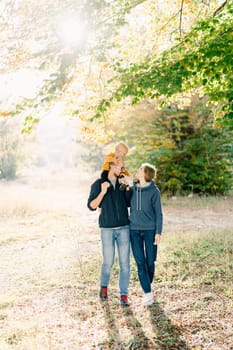 Mom hugs dad with a little boy on his shoulders, walking in the autumn park. High quality photo