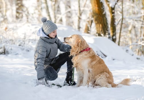 Teenage Girl And Golden Retriever Sit Together In Snow-Covered Forest During Winter