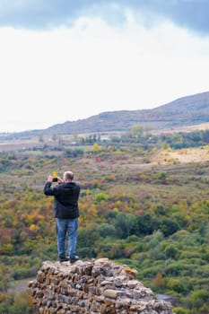 Man taking pictures of mountains while standing on the ruins of a wall