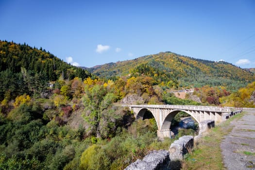 An awe-inspiring tall bridge extends over a picturesque river within the breathtaking mountainous region. The sight evokes a sense of adventure and exploration.
