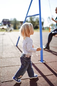 Little girl goes to the swing with her mother sitting. Side view. High quality photo