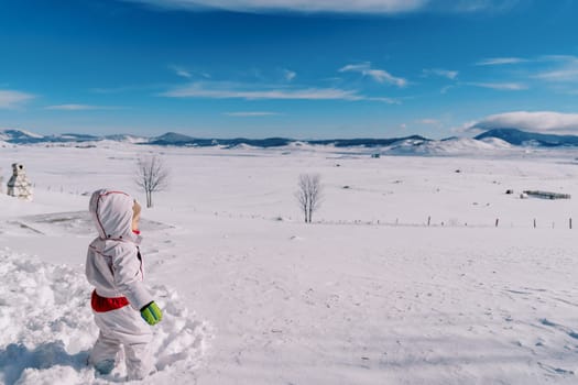 Little girl stands in a deep snowdrift in a mountain valley and looks into the distance. Side view. High quality photo