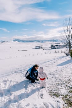 Small child stands next to his father, who is squatting in the snow, and looks at him. Back view. High quality photo