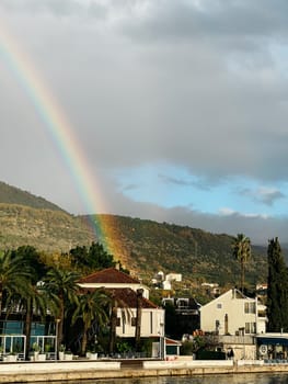 Colorful rainbow over the houses on the sea coast at the foot of the mountains. High quality photo