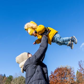 More, more,...mum, that's fun. Happy young mother throws her cute little baby boy up in the air. Mother's Day, Mather and her son baby boy playing and hugging outdoors in nature in fall