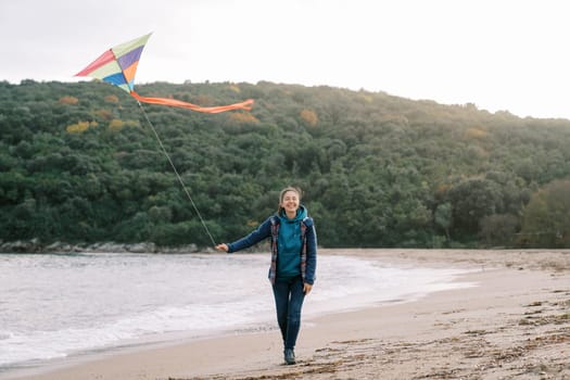 Smiling woman walking along the seashore with a colorful kite on a string. High quality photo