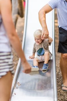 Parent hand holding little infant baby boy child while sliding on urban playground on a sunny summer day. Family joy and happiness concept.