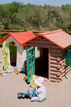 Little girl plays with a toy car near plastic houses on the playground. Back view. High quality photo