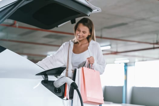 Young woman travel with EV electric car to shopping center parking lot charging in downtown city showing urban sustainability lifestyle by green clean rechargeable energy of electric vehicle innards