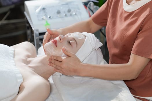 Portrait of beautiful caucasian woman having facial massage with homemade facial mask while lies on spa bed surrounded by beauty electrical equipment and peaceful nature environment. Tranquility.