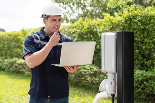 Qualified technician working on home EV charging station installation, making troubleshooting and configuration setup on charging system with laptop for EV at home. Synchronos