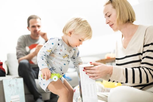 Cute little blond Caucasian toddler unpacking Christmas or Birthday present. Adorable small infant baby boy opening gift.