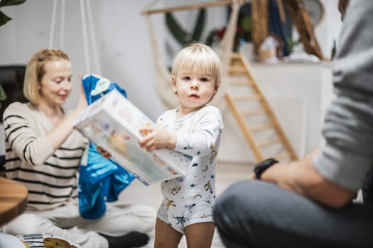 Cute little blond Caucasian toddler unpacking Christmas or Birthday present. Adorable small infant baby boy opening gift.