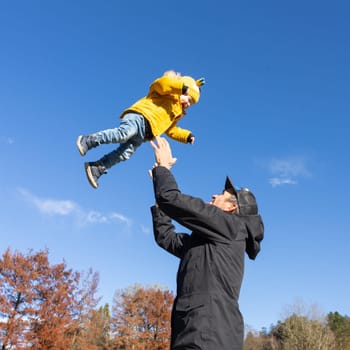 More, more,... dad, that's fun. Happy young father throws his cute little baby boy up in the air. Father's Day, Father and his son baby boy playing and hugging outdoors in nature in fall