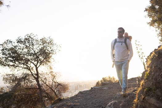 Young father carrying his infant baby boy son in backpack while tracking around Malaga, Spain in sunset. Family travel and vacation concept.