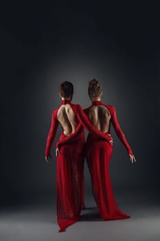 Back view of elegant dancers in long lace dresses, on gray backdrop