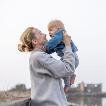 Tender woman caressing her little baby boy infant child outdoors on autumn trip to Secovlje salinas landscape park, Slovenia. Mother's unconditional love for her child