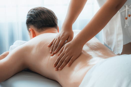 Caucasian man customer enjoying relaxing anti-stress spa massage and pampering with beauty skin recreation leisure in day light ambient salon spa at luxury resort or hotel. Quiescent