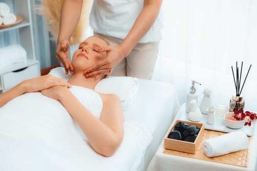 Caucasian woman enjoying relaxing anti-stress head massage and pampering facial beauty skin recreation leisure in dayspa modern light ambient at luxury resort or hotel spa salon. Quiescent