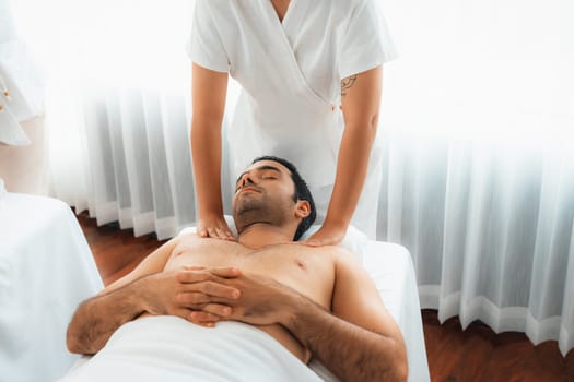 Caucasian man customer enjoying relaxing anti-stress spa massage and pampering with beauty skin recreation leisure in day light ambient salon spa at luxury resort or hotel. Quiescent