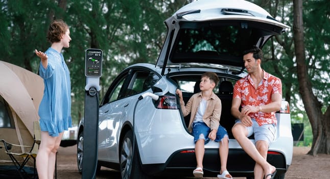 Outdoor adventure and family vacation camping in nature travel by eco friendly car for sustainable future. Lovely family recharge EV car with EV charging station in campsite. Perpetual